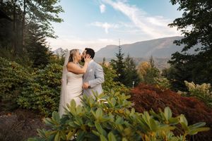 A couple embraces amid vibrant autumn foliage with mountains and trees creating a scenic outdoor backdrop.