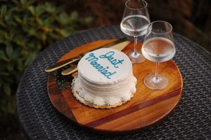 A rustic wooden serving board with wine glasses and a decorated cake on a textured dark surface.