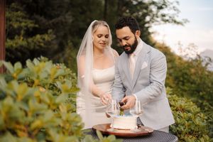 A couple celebrates their wedding with a delicate floral cake set against a lush garden backdrop during golden hour.