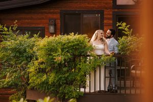 A couple shares a romantic moment on a balcony surrounded by lush greenery and plants at sunset.