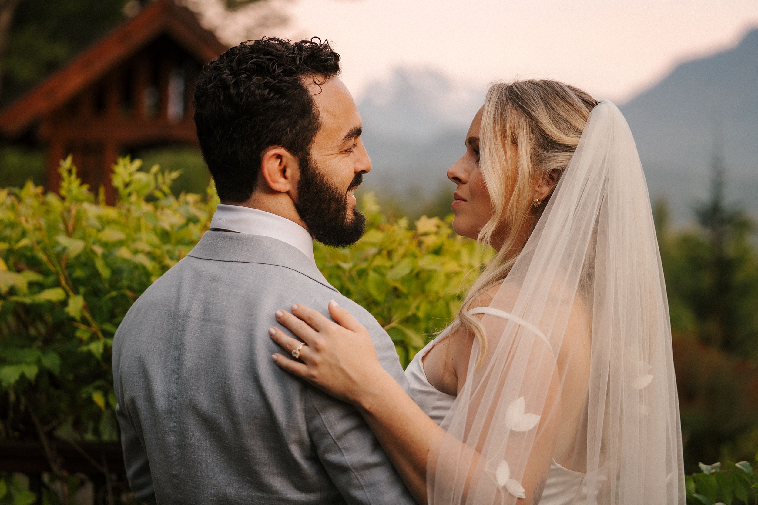 A couple shares an intimate moment during their outdoor wedding photoshoot against a scenic mountain backdrop.