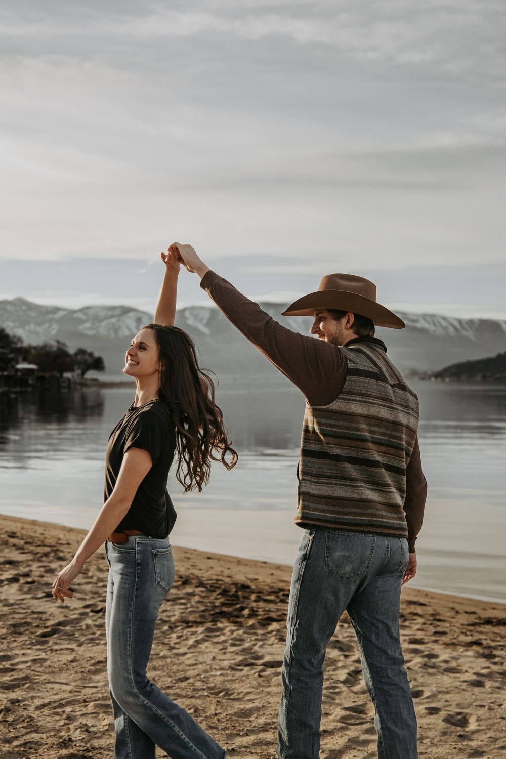 Couple dancing together on a beach with mountains and lake in the background.