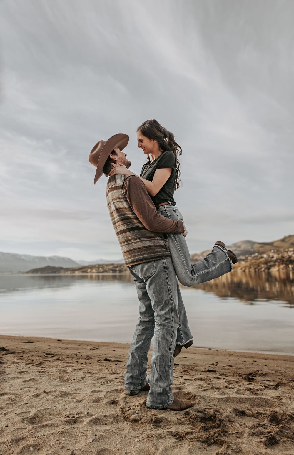Romantic couple embracing on a beach with mountains and lake in the background.