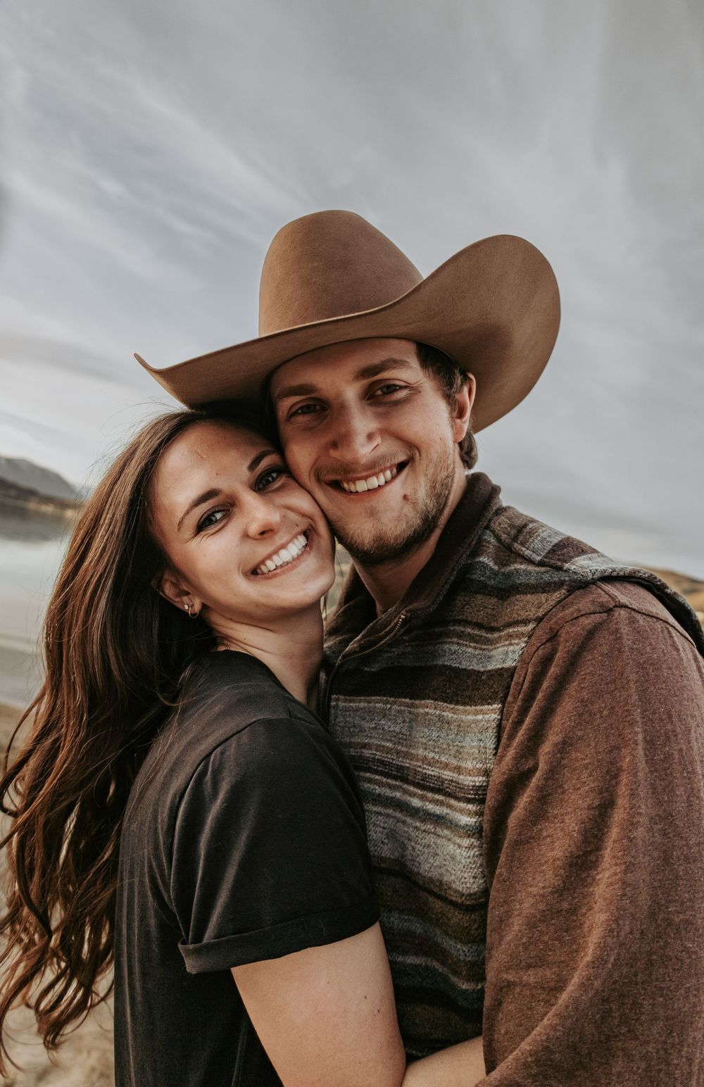 Happy couple posing for a close-up photo on beach with mountains in background.