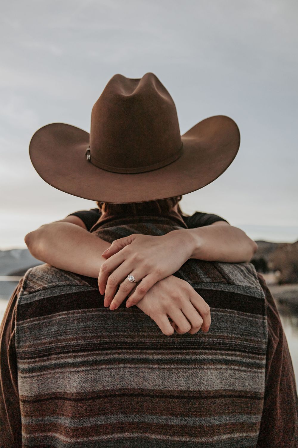 Close-up view of hands resting on a striped western shirt with a brown cowboy hat.