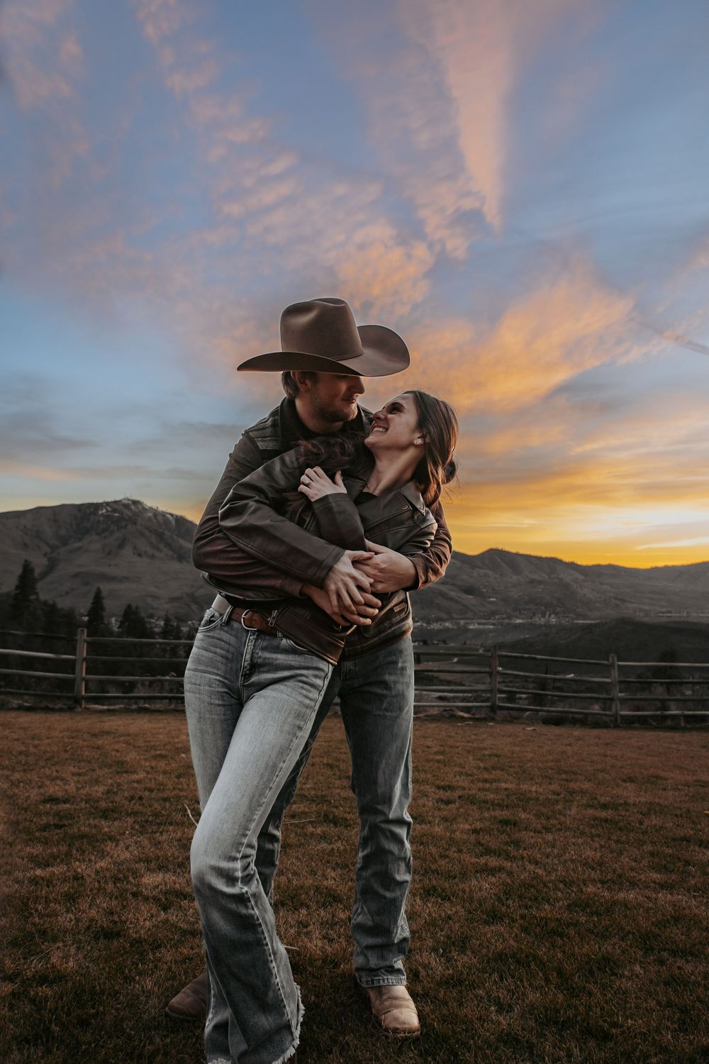 Couple sharing an intimate moment at sunset in a rustic mountain field.