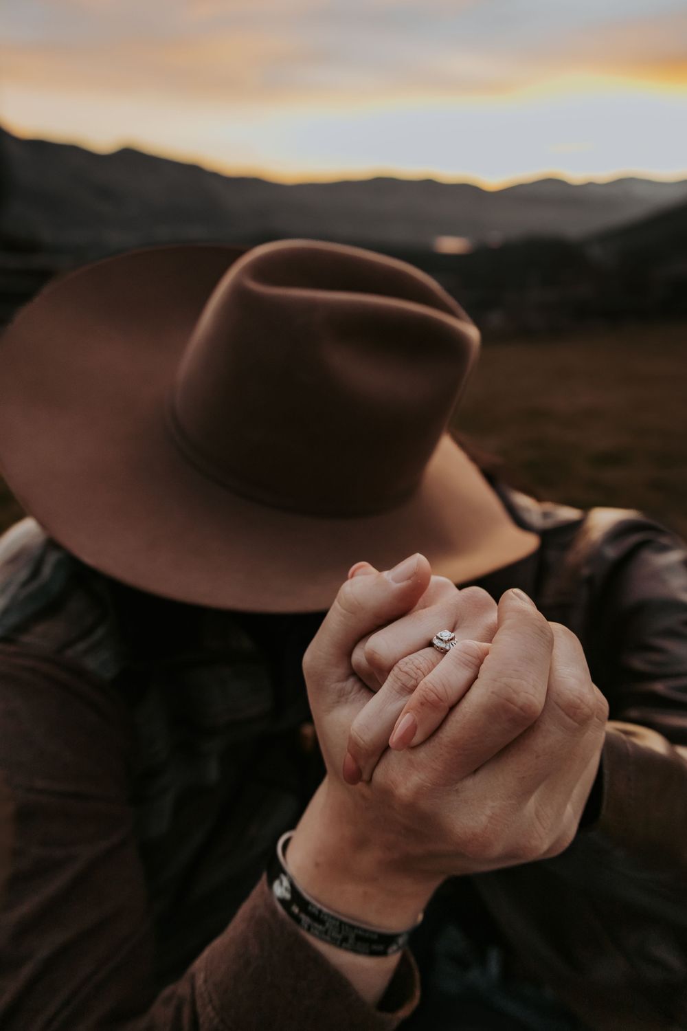 Close-up of intertwined hands against a mountain sunset backdrop.