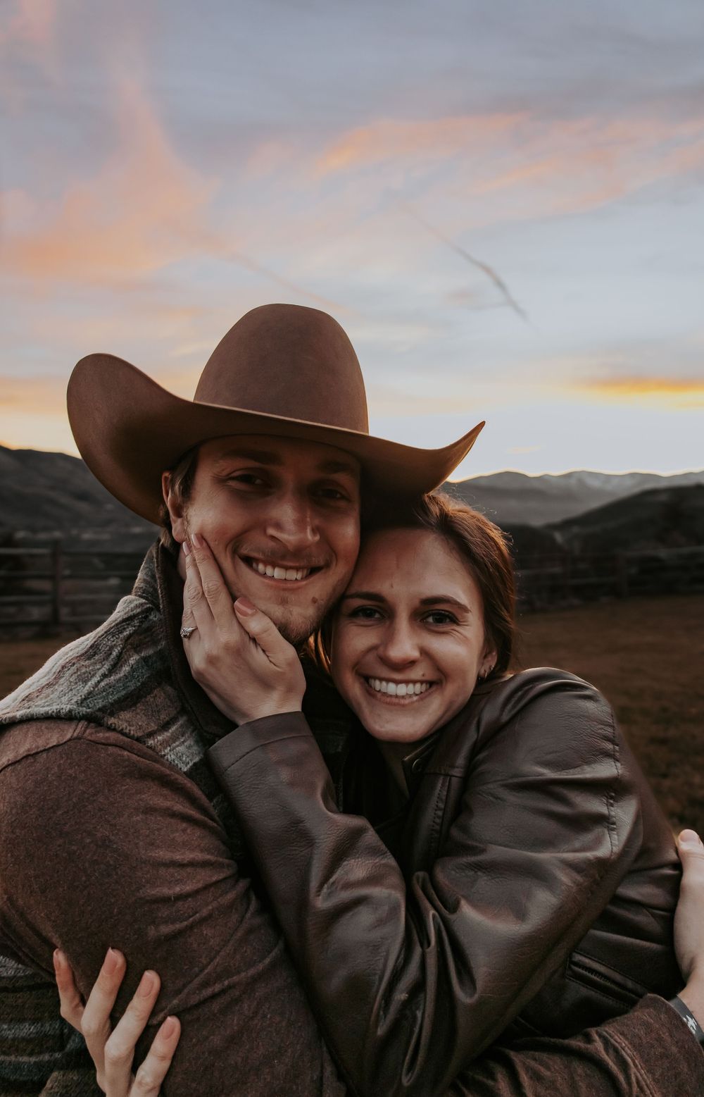 Couple in western wear sharing joyful laughter during sunset in the mountains.