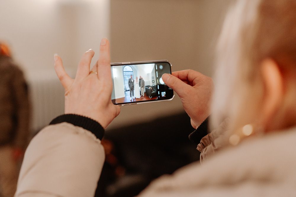 People sharing emotional moments and embracing at a wedding ceremony while someone captures photos on a phone.