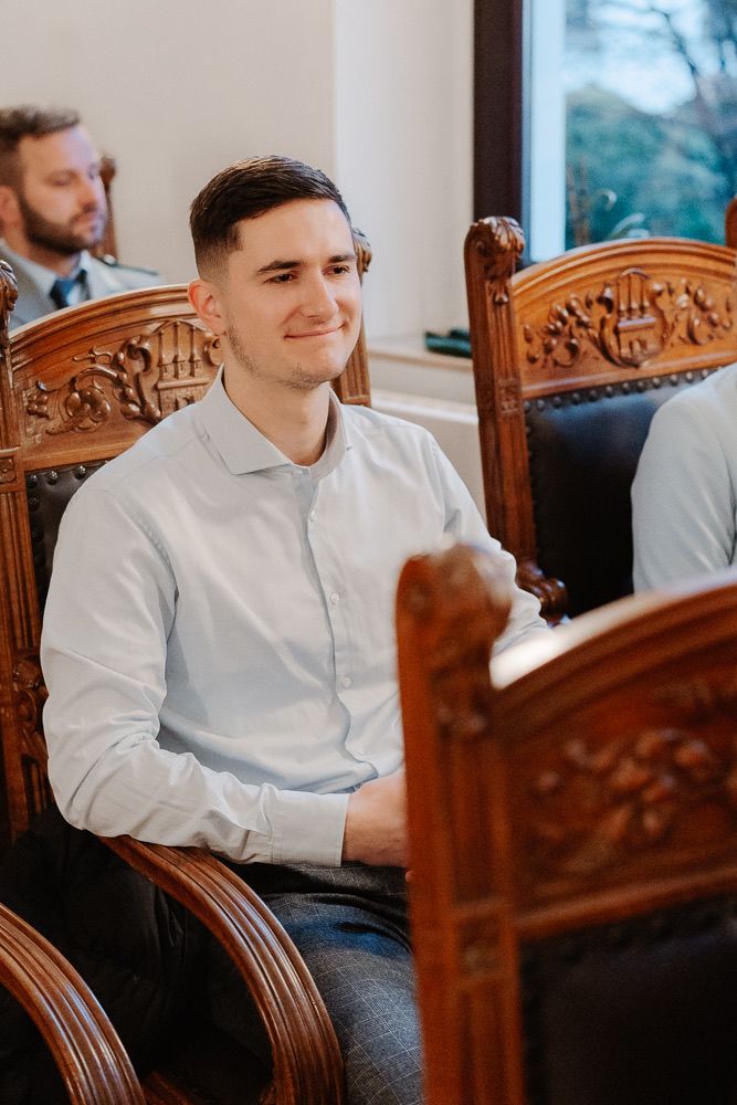 People seated in ornate wooden chairs with carved details during an indoor event.