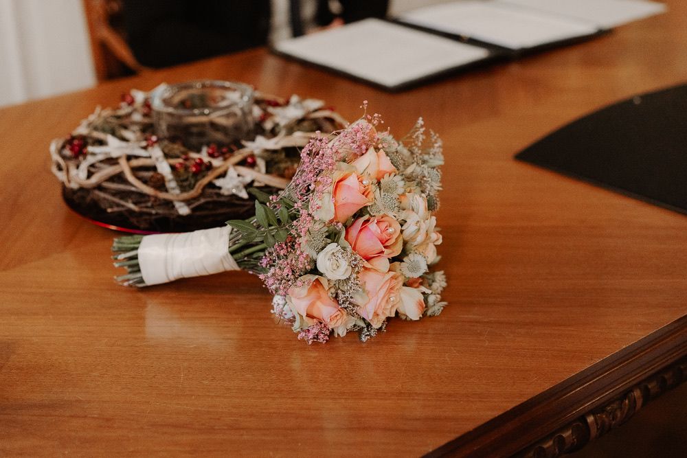 A wooden table surface holds a decorative floral arrangement with pink and white flowers and greenery.