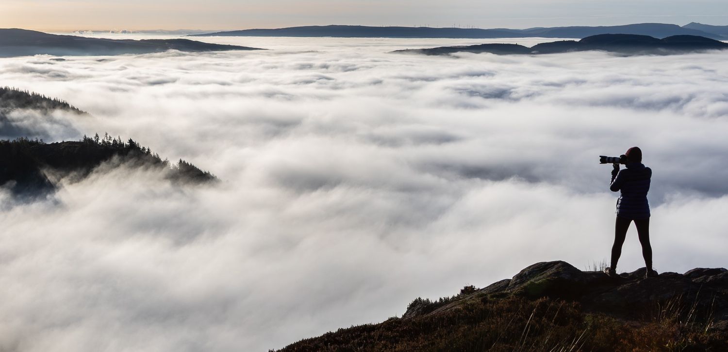 Silhouetted figure stands on mountain ridge overlooking sea of clouds at sunrise.
