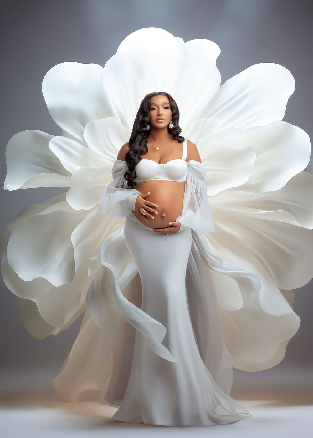 Pregnant woman in white maternity gown with dramatic flowing petal-shaped fabric wings on gray backdrop.
