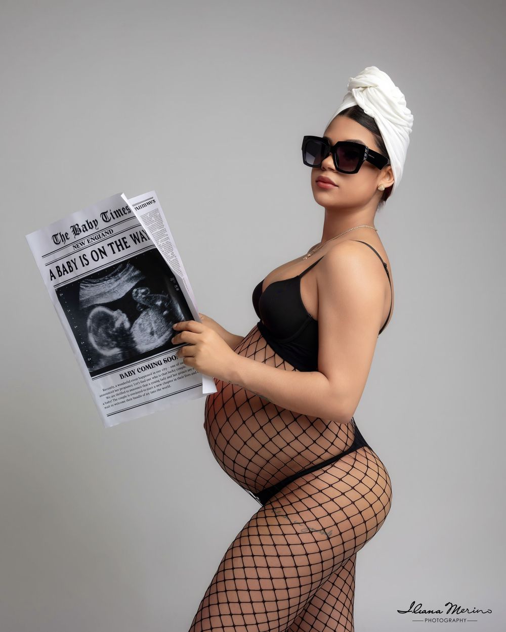 Side profile of pregnant woman in fishnet tights holding Baby Times newspaper in creative maternity photo.