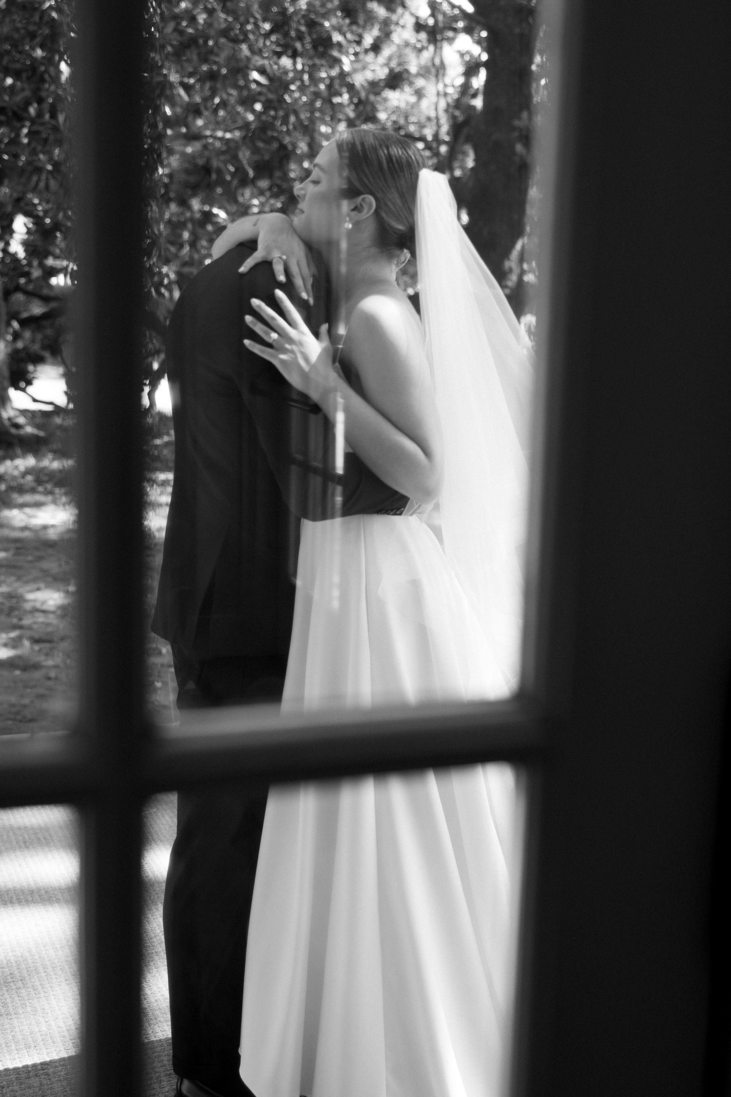 Wedding party members in formal attire help adjust a bride's flowing white dress on a grassy lawn.
