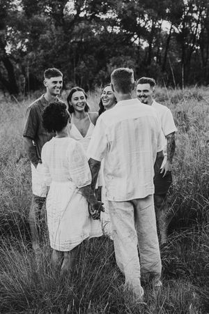 Black and white photo of a group of young adults laughing and holding hands in a grassy field.