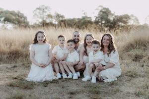 Family group sitting together in coordinated outfits on grass during golden hour.