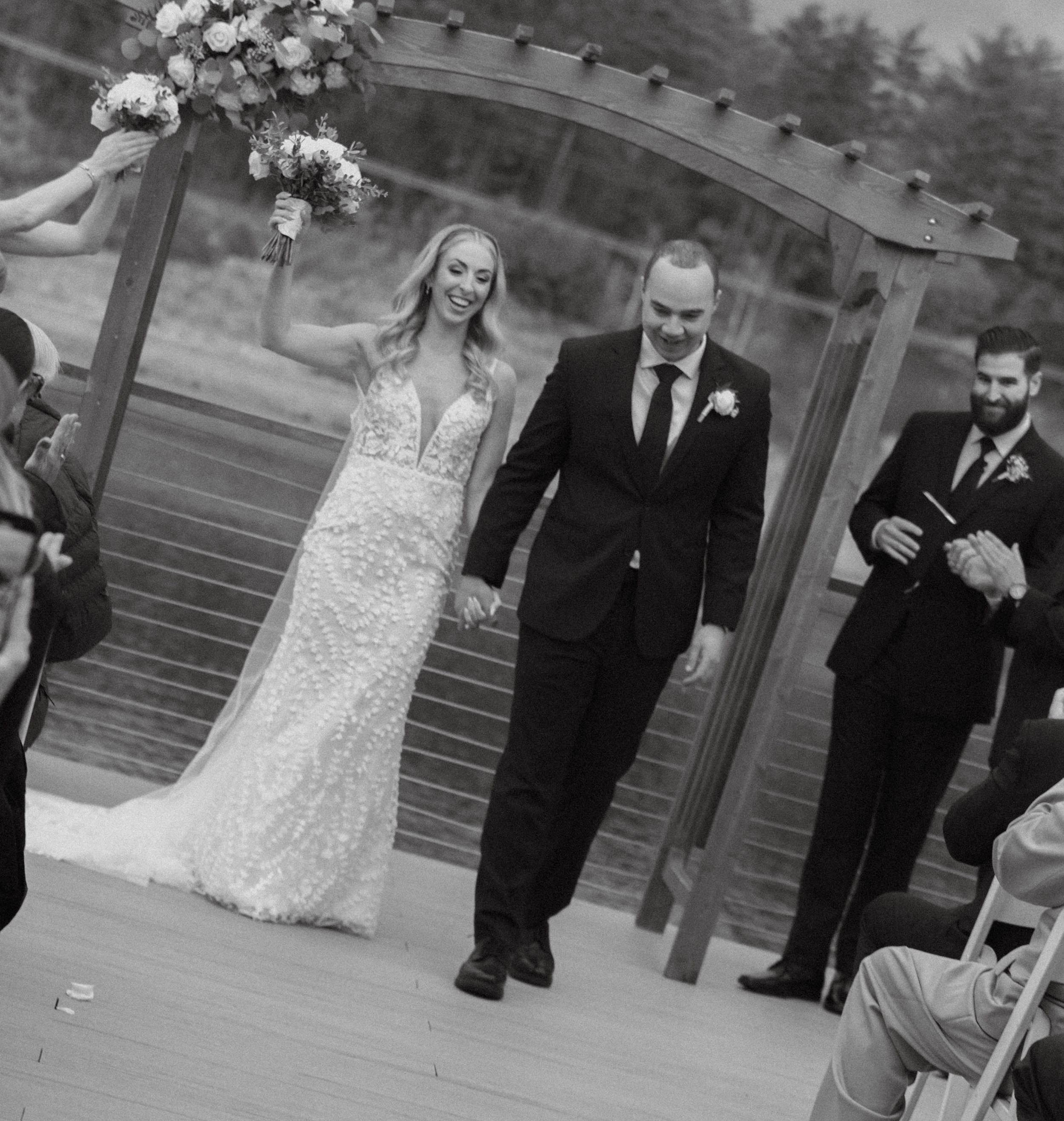 Black and white photo of smiling bride and groom walking down the aisle after ceremony.