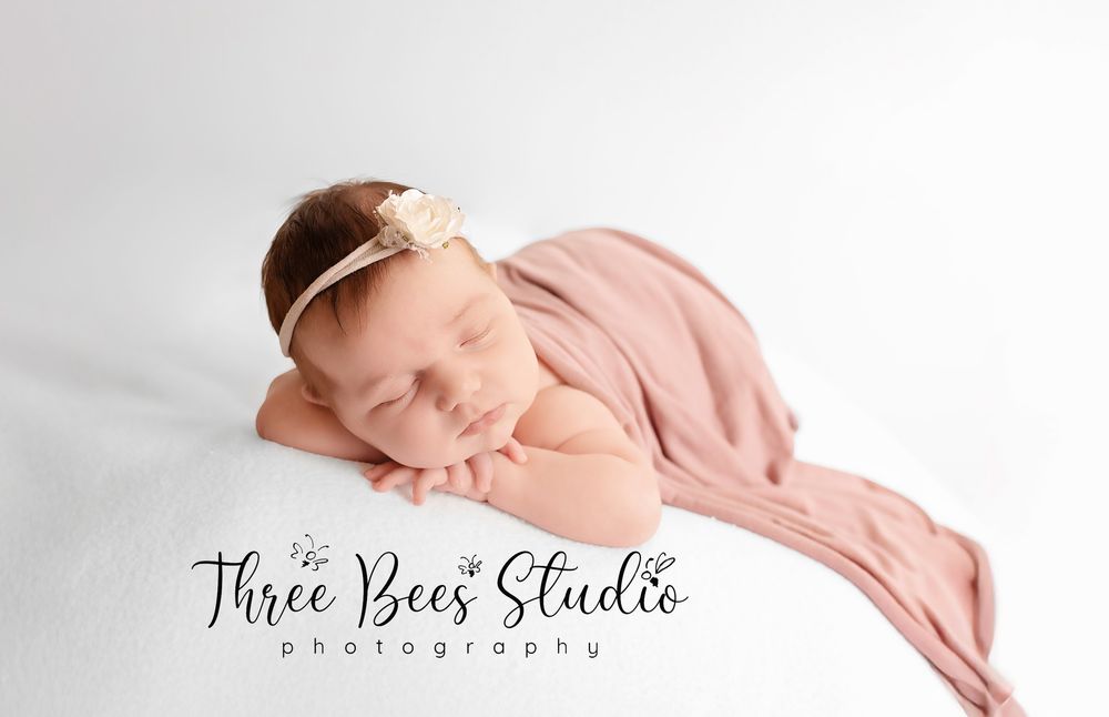 Peaceful sleeping newborn wrapped in soft pink fabric on white backdrop with studio photography text overlay.