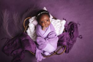 Newborn photography with purple fabric and feather decorations on purple background.