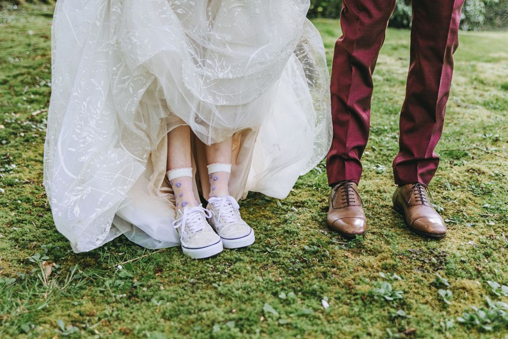 Wedding shoes detail shot showing sneakers and dress shoes on grass.