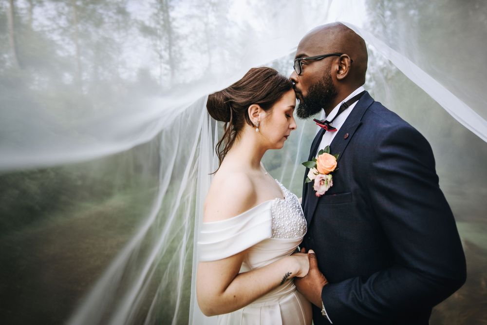 A romantic wedding portrait with flowing veil creating an ethereal atmosphere.
