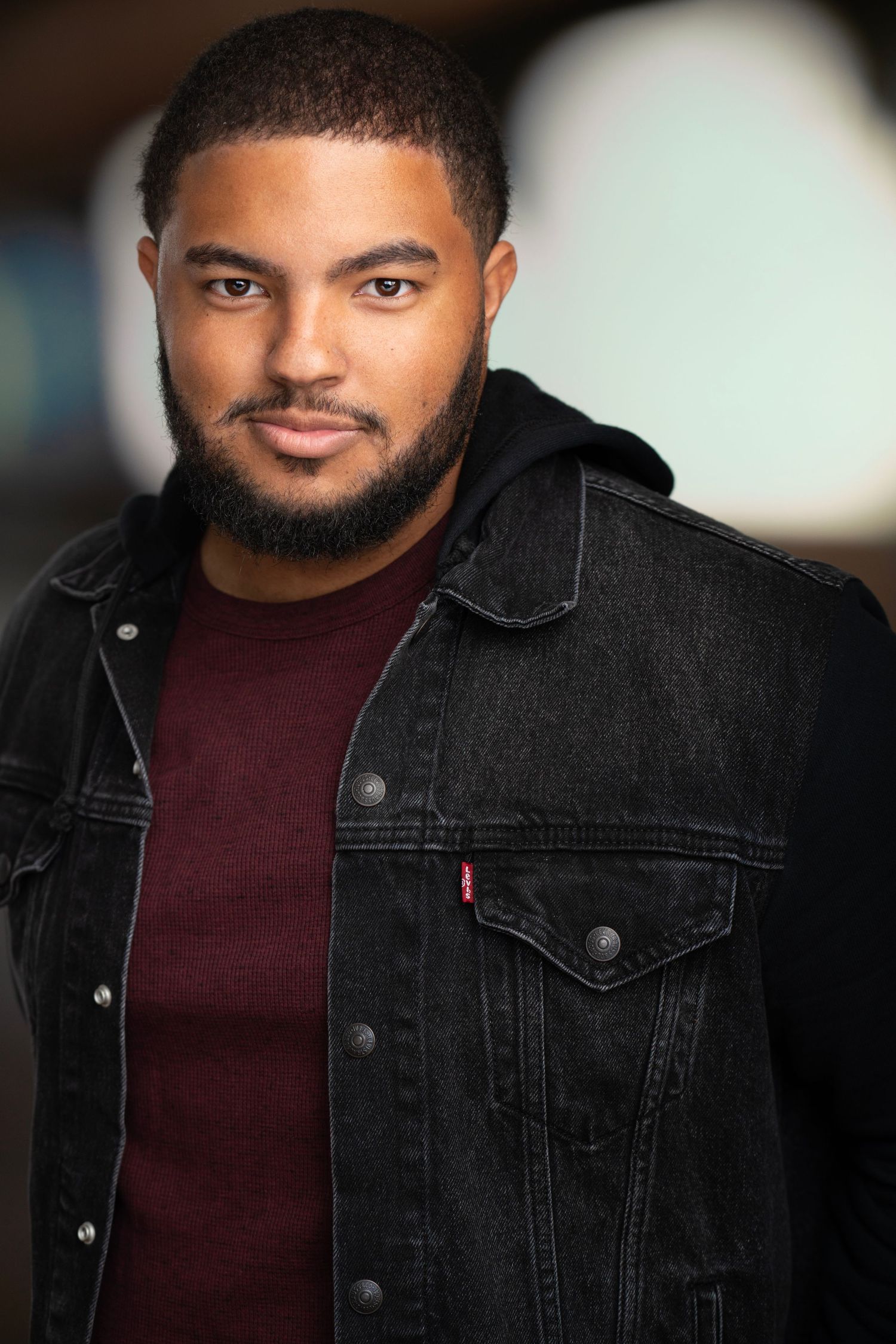Professional headshot of a man wearing a black denim jacket and burgundy shirt.