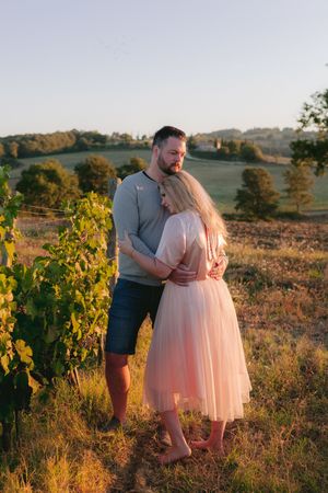 Couple embracing in golden sunlight amid rolling hills and autumn vineyard at sunset.