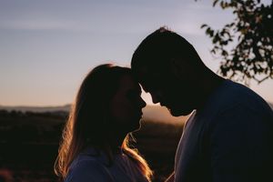 Silhouetted couple sharing intimate moment at sunset with sun rays illuminating their outlines.