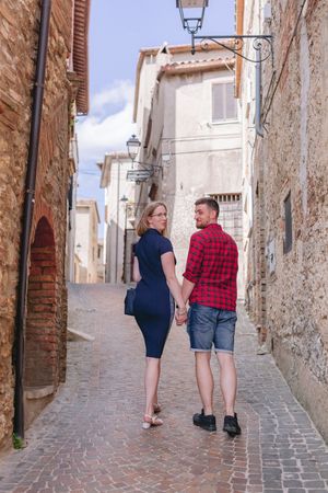 A couple walking hand in hand through a narrow cobblestone street in an old Italian village.