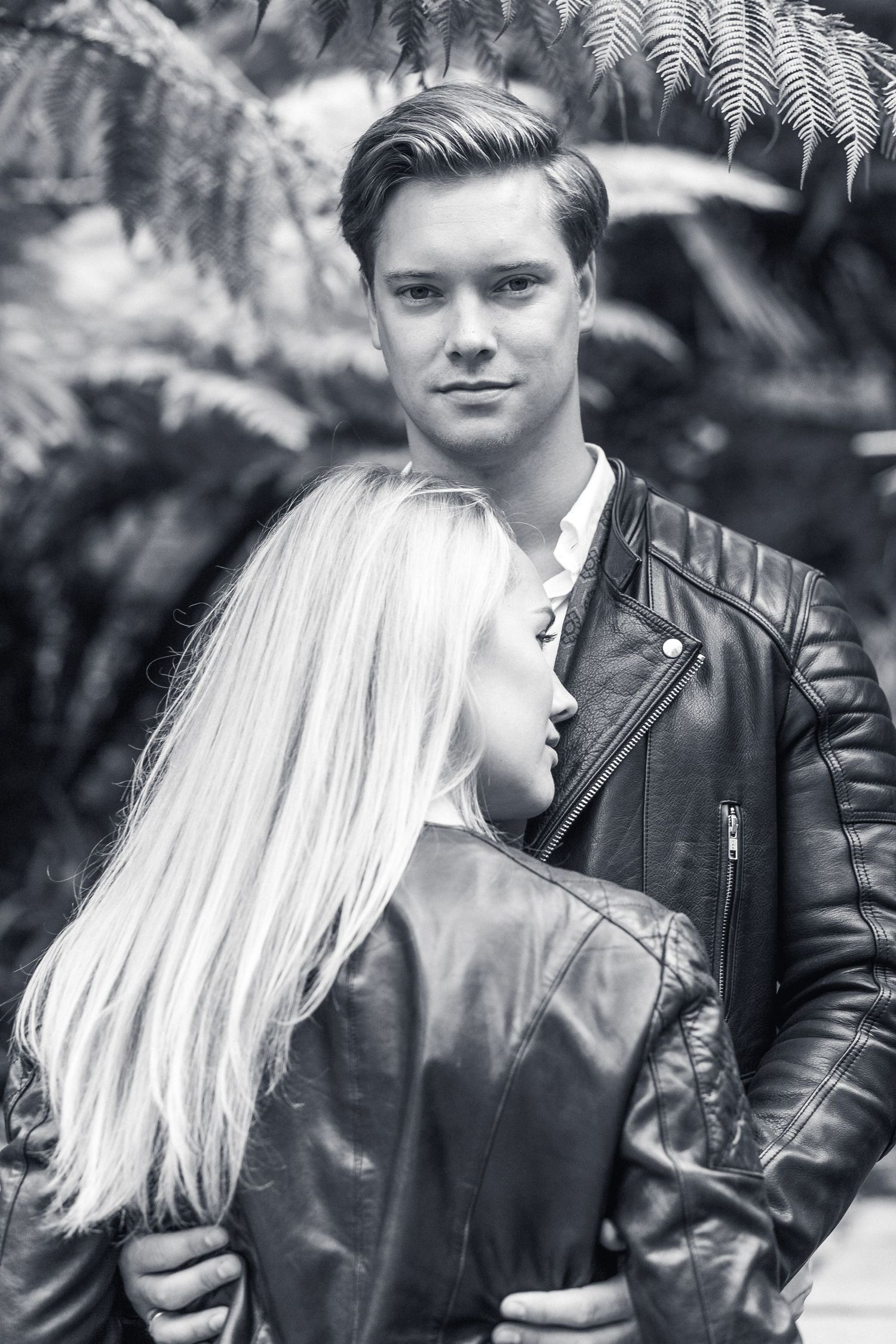 Romantic black and white portrait of a couple posing together, with ferns in the background.