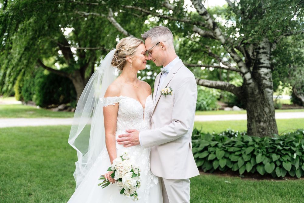 Bride and groom share a romantic moment outdoors, with bride in off-shoulder gown holding white bouquet.