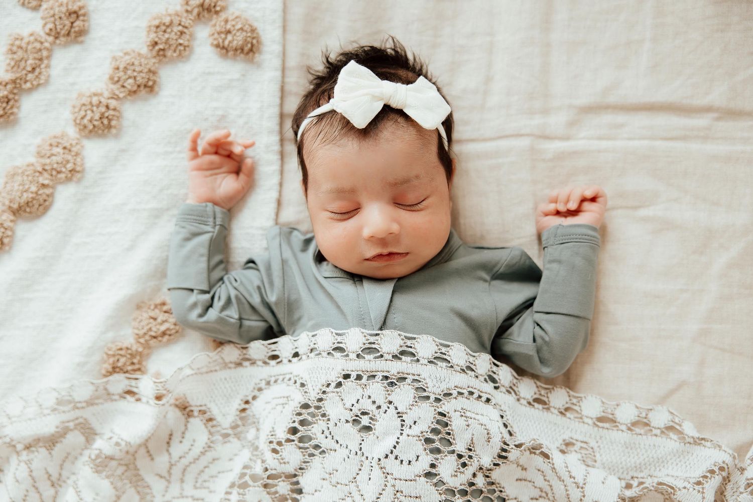 Peaceful newborn baby girl in grey outfit and white bow headband sleeping on textured blanket in a lifestyle studio in Vancouver.