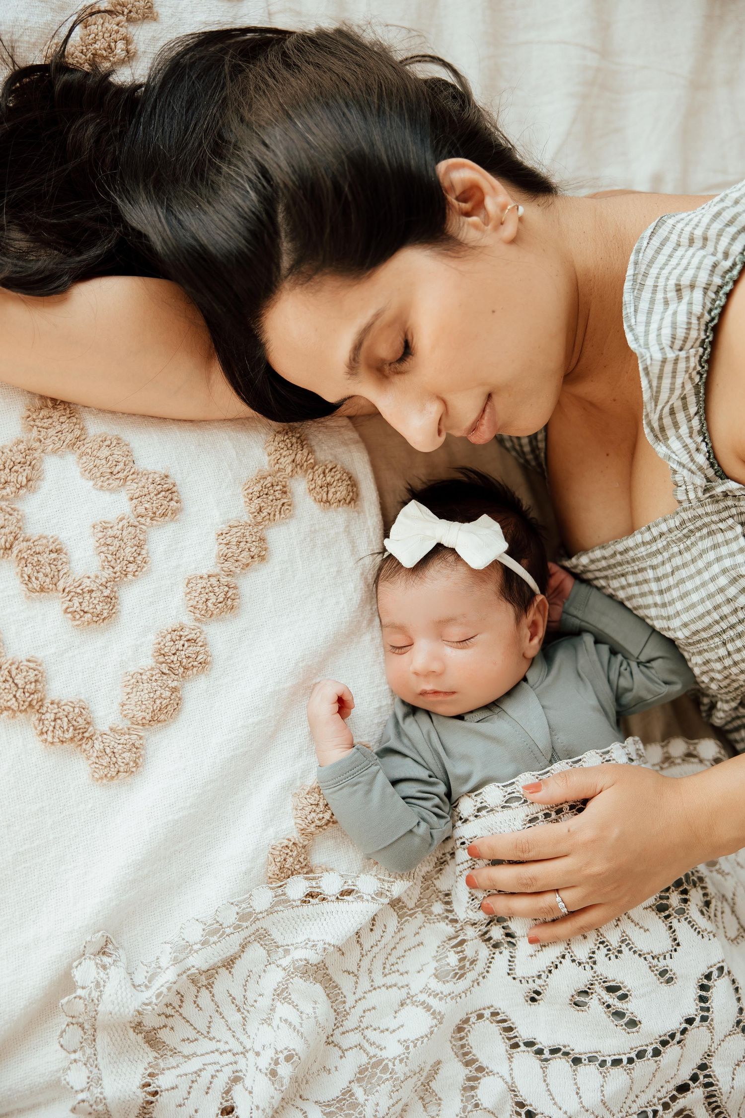 Mother with dark hair lying beside her sleeping newborn baby girl on a decorative blanket in a lifestyle studio in Vancouver.