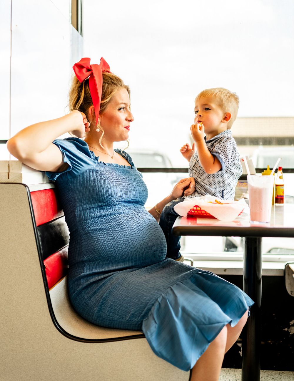 Playful poses in vintage-inspired diner setting with blue dress.