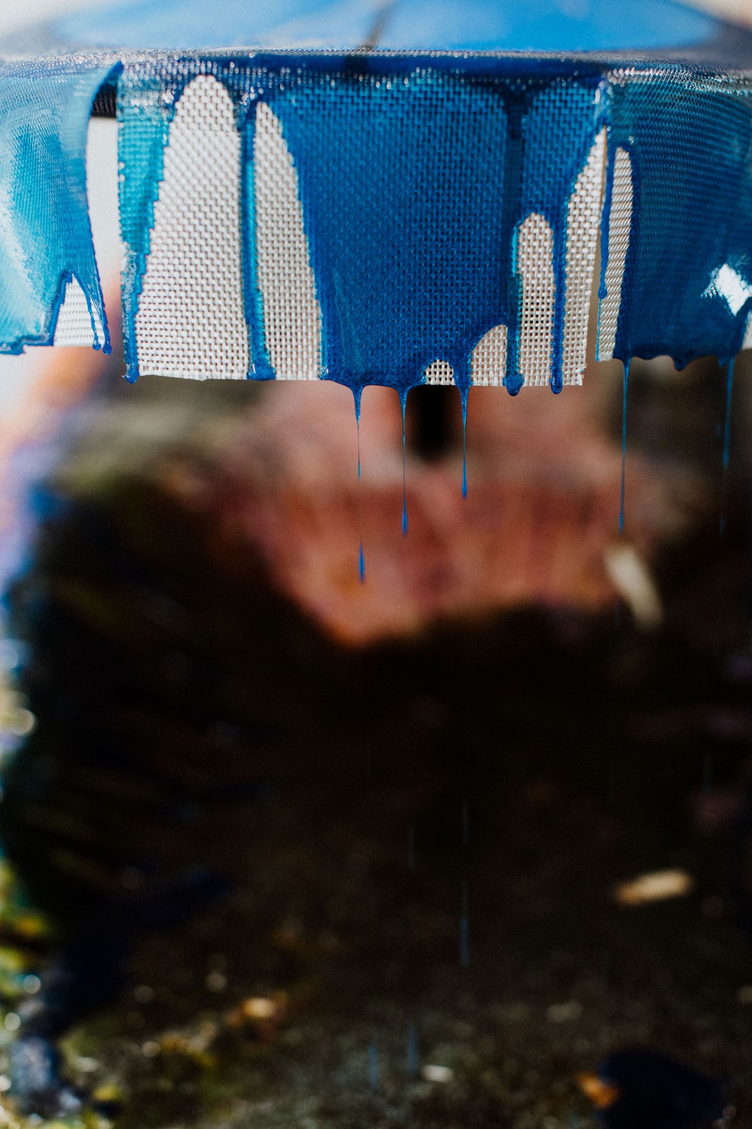 Photographie d'une planche de surf en gros plan, dans l'atelier de stratification, la résine teintée bleu dégouline sur le tissu