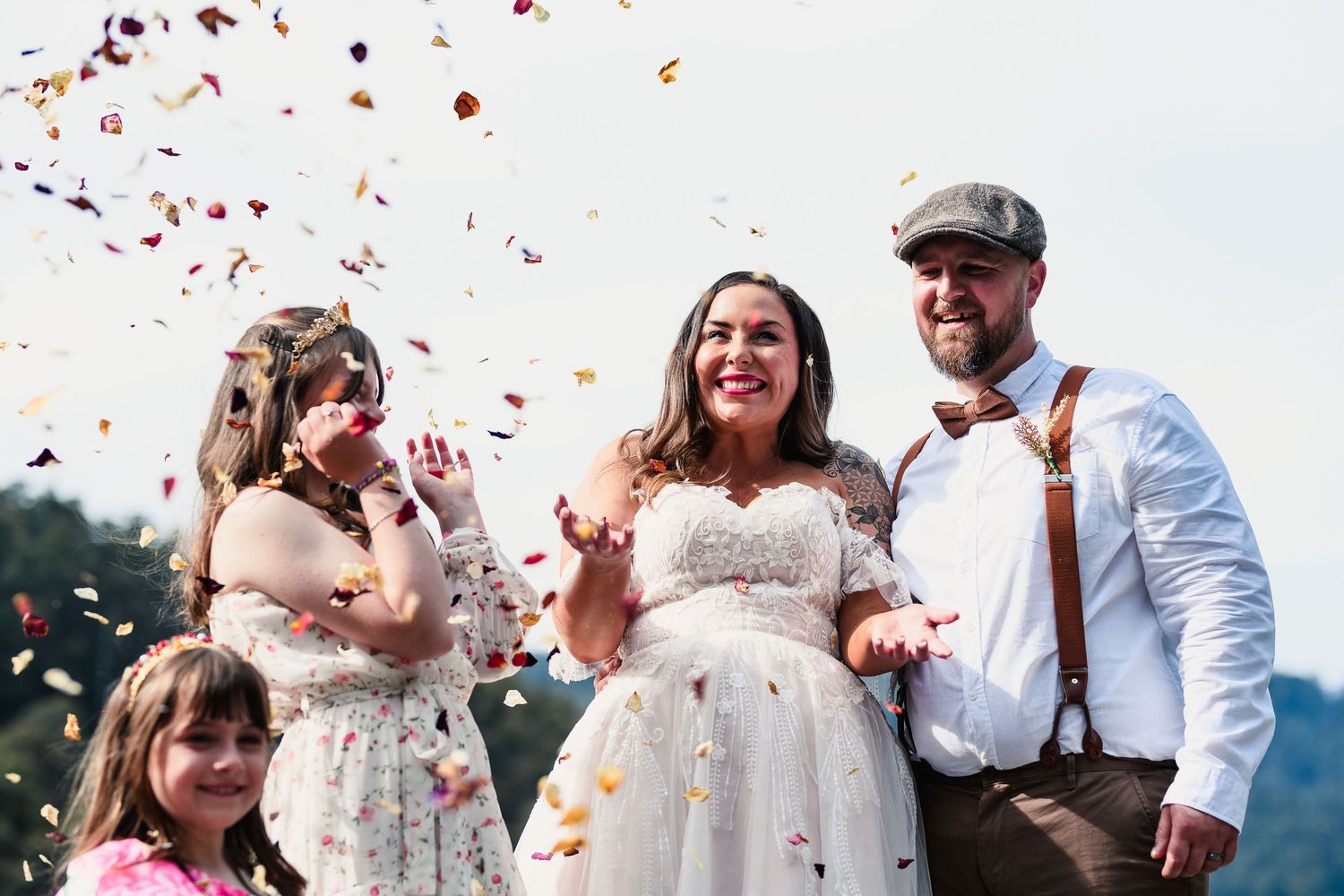 A joyful celebration outdoors as confetti falls through the air during a sunny wedding ceremony.