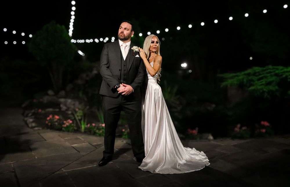 Evening wedding portrait with string lights glowing in garden backdrop.
