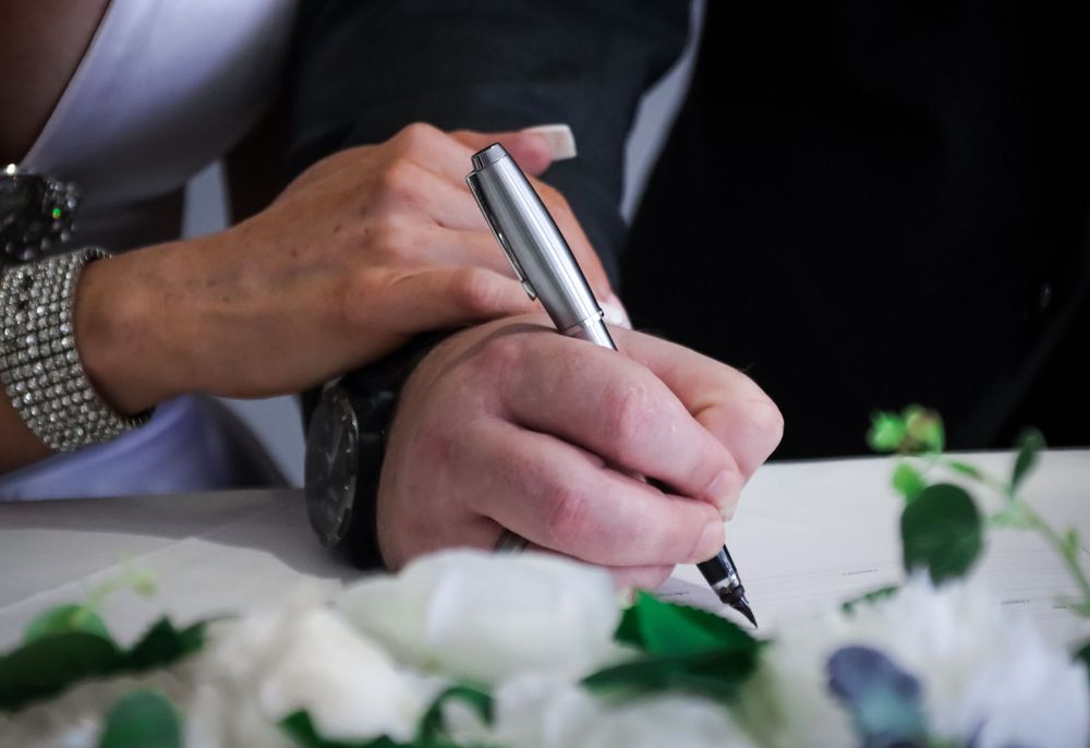Close-up of hands signing wedding document with pen.