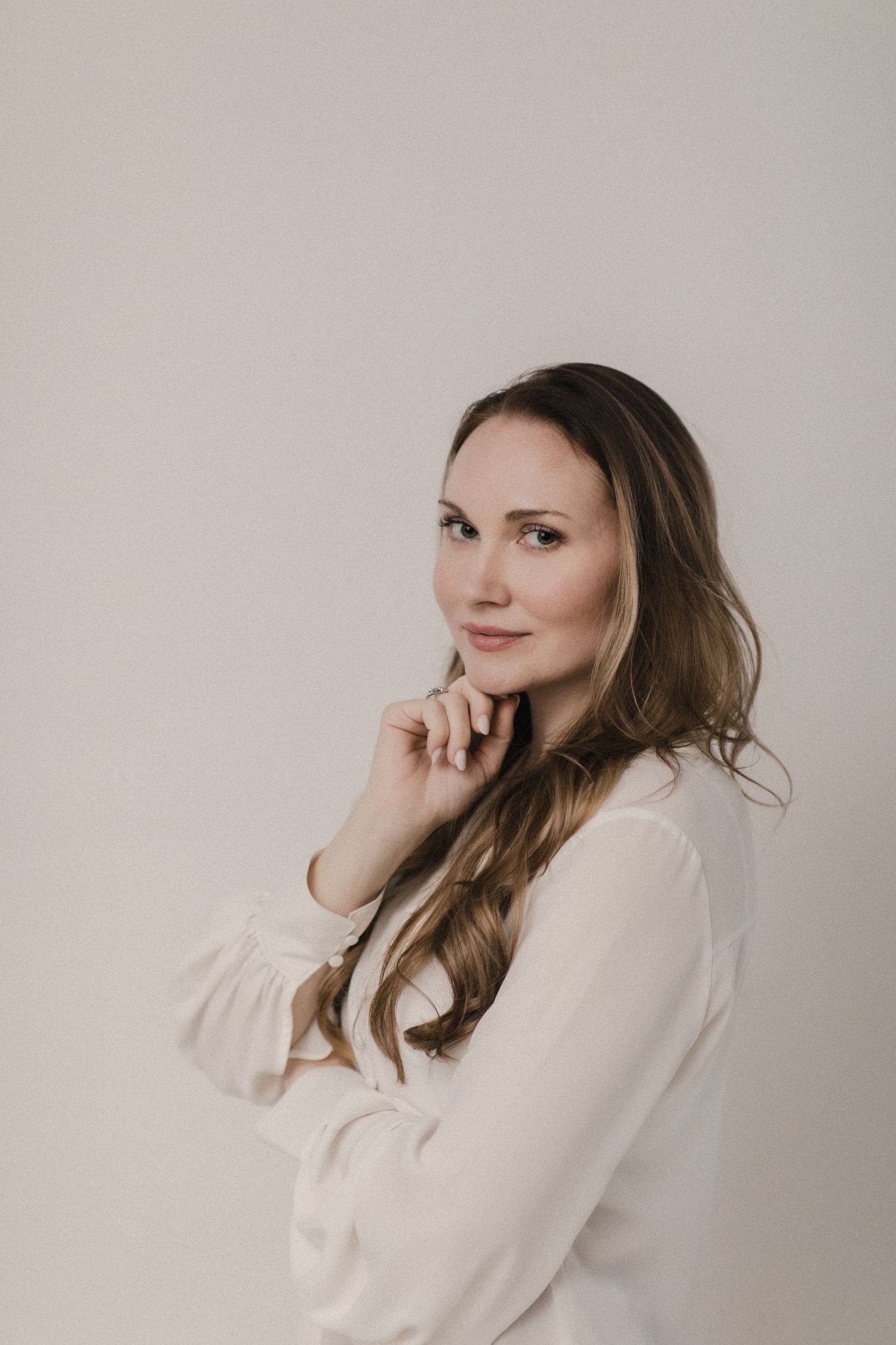 Portrait of Heather Cahoon with long brown hair wearing a white blouse against a neutral background posing thoughtfully.