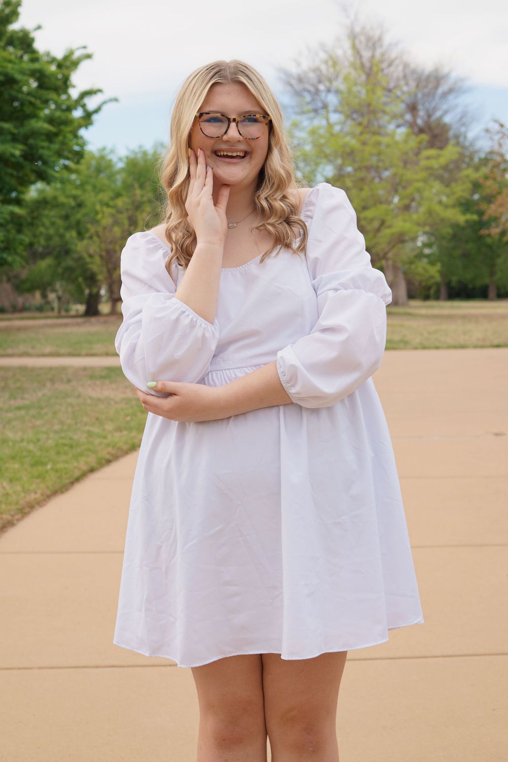 Portrait of person in white puff sleeve dress and glasses standing on concrete path.