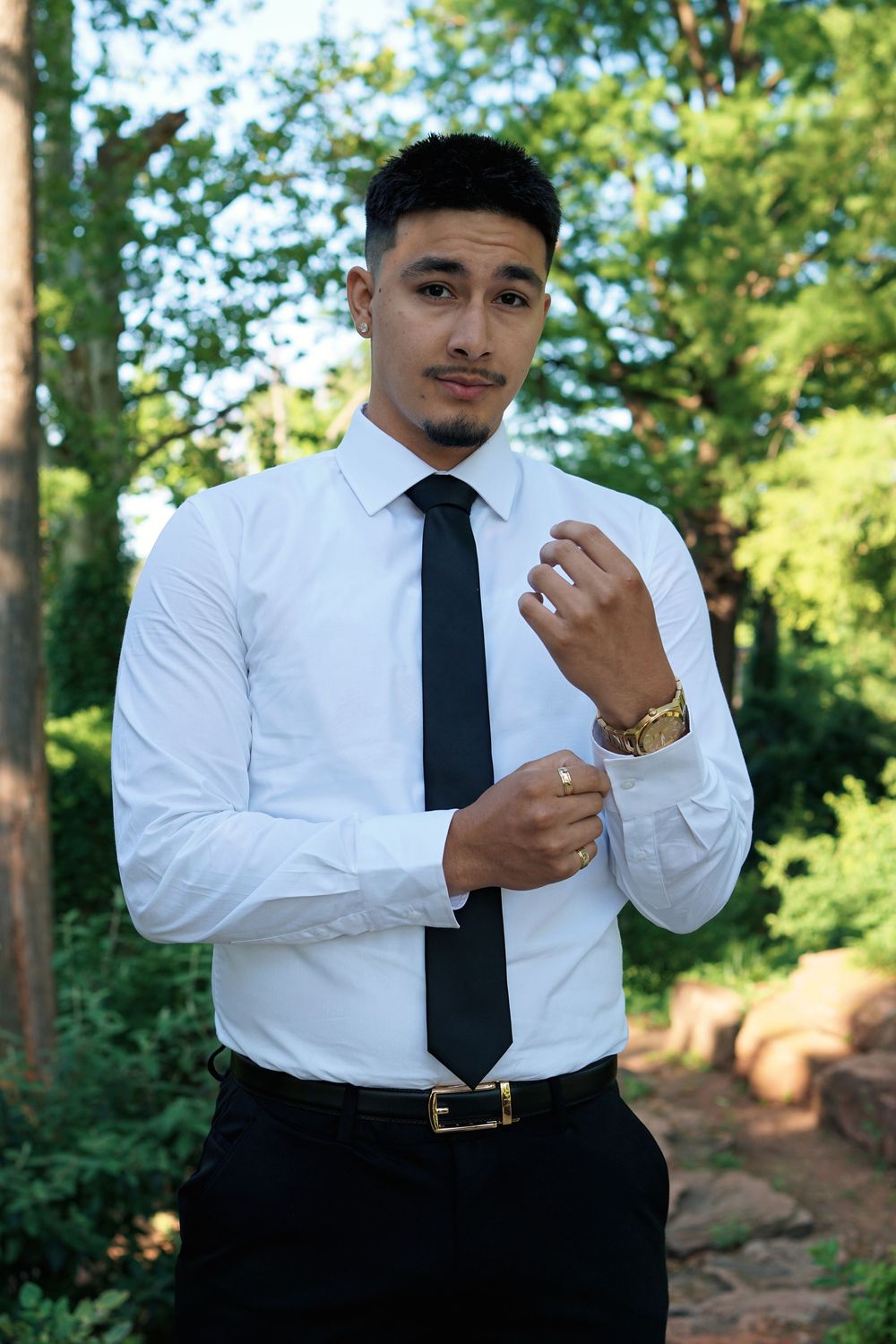 Professional portrait of someone adjusting shirt cuffs while wearing a crisp white dress shirt, black tie and gold watch.