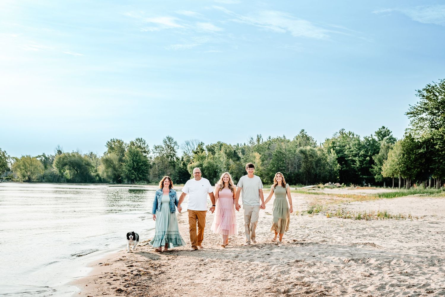 Group walking together holding hands along a scenic beach shoreline on a sunny day.