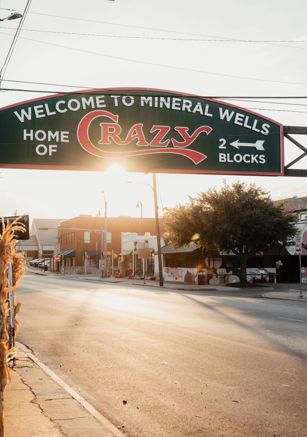 Welcome sign to Mineral Wells featuring Crazy Blocks spans over a street at sunset with golden light illuminating the scene.