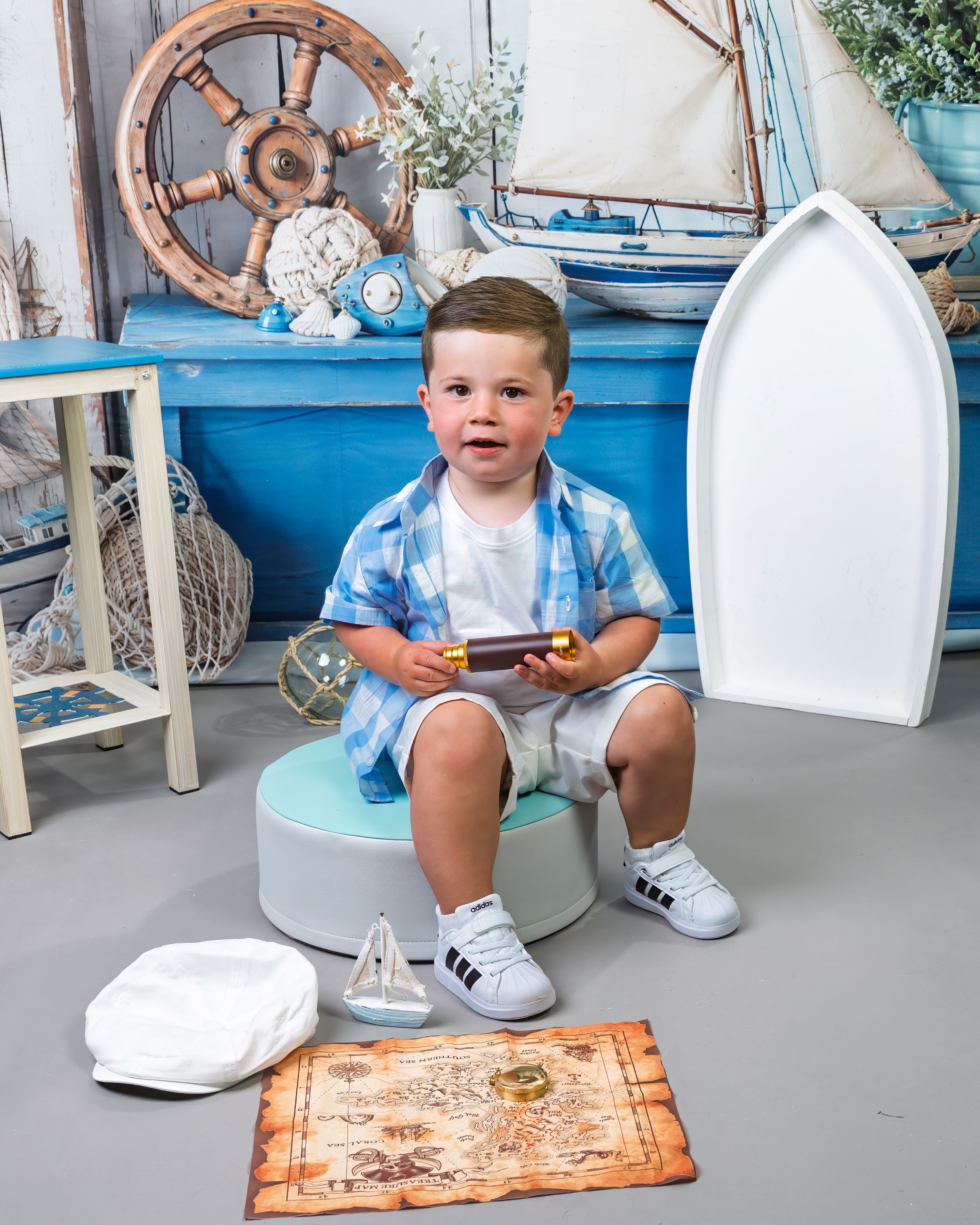 Young boy sits on a blue potty chair holding a toy in a nautical-themed photo studio backdrop setting.