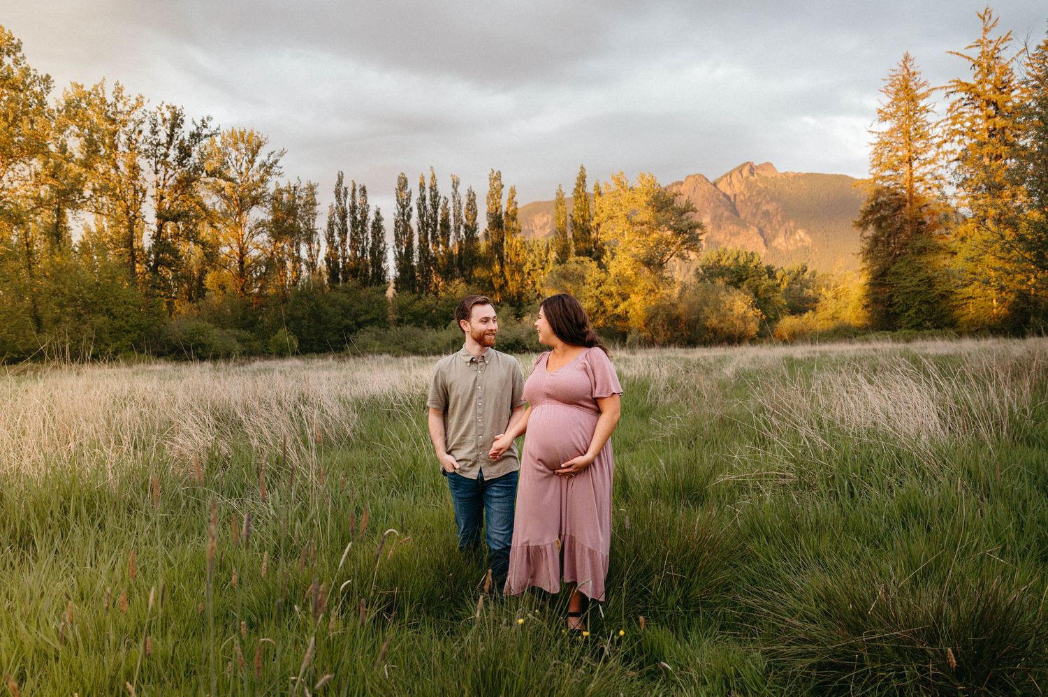 A scenic family photoshoot in a golden field during sunset with mountains in the background.