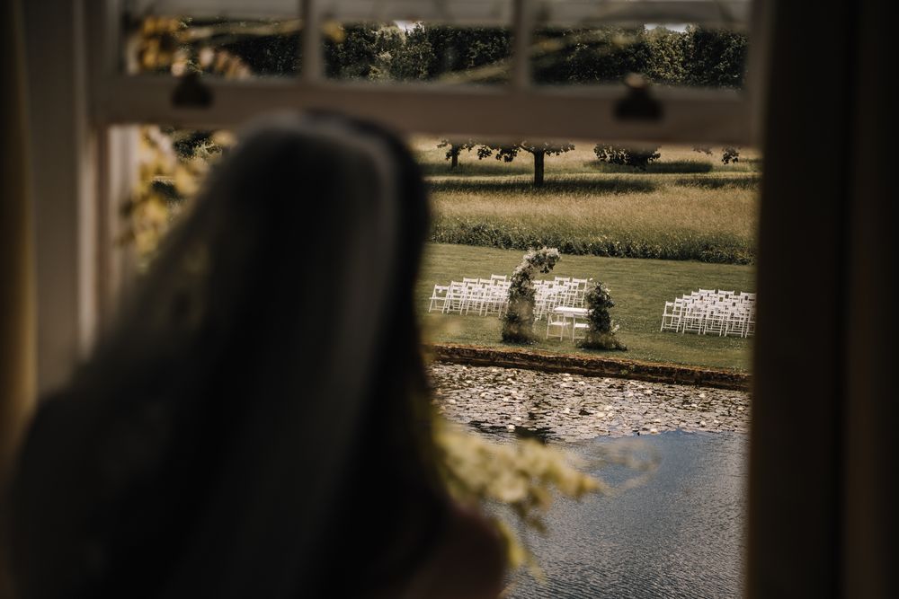 View through a window of an outdoor wedding ceremony setup with white chairs on a lush green lawn.