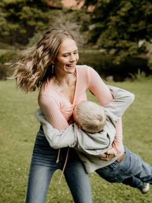Playful moment captured as person in pink sweater swings child in casual outdoor setting.