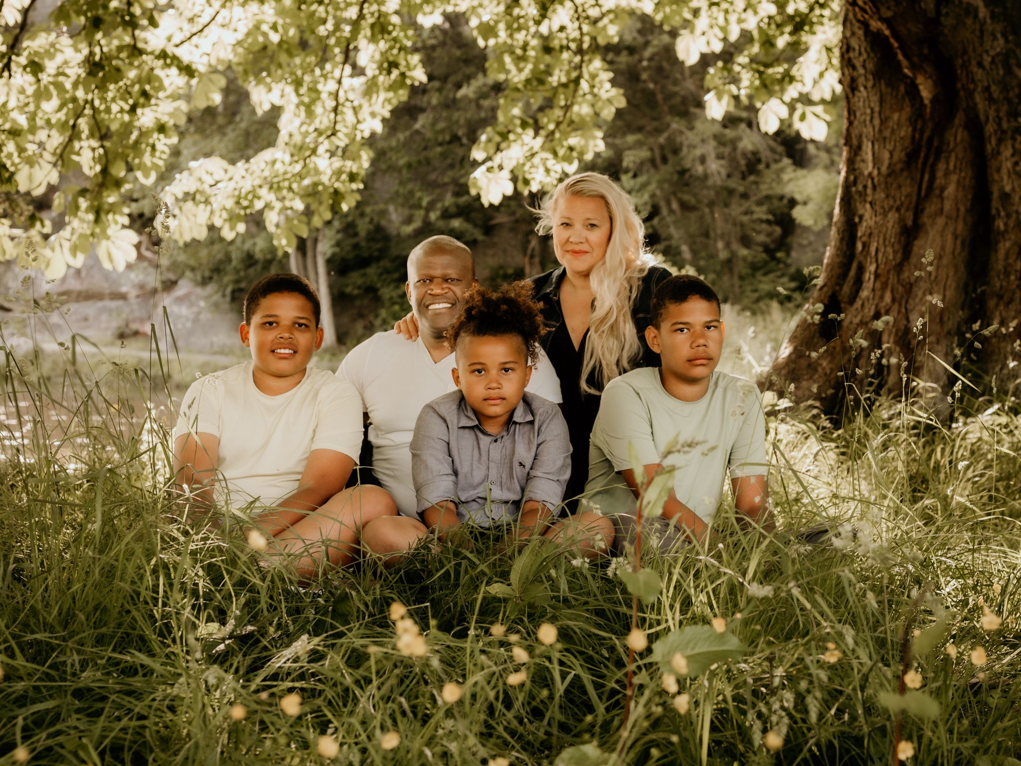 Sun-drenched family portrait in flowering meadow with white blossoms.