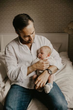 A parent in white shirt and jeans holds and comforts their infant on a bed in a series of intimate photos.